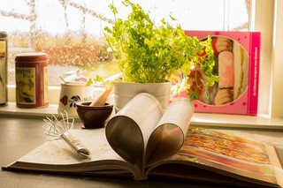 open cookbook on kitchen counter with herbs in the background